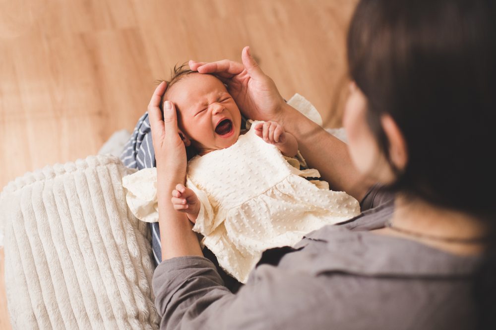 Crying baby girl wake up on mother hands in room closeup. Woman with infant girl. Motherhood. Childhood.