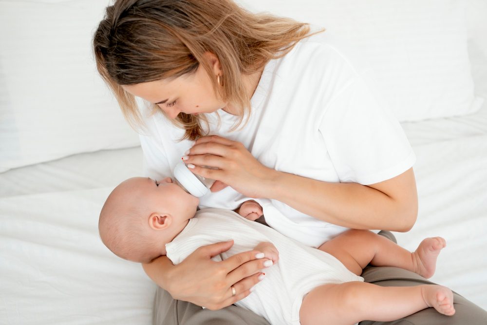 mom feeds the baby with a bottle of milk or formula, feeding the baby in her arms, a young mother feeds the newborn baby at home on the bed.