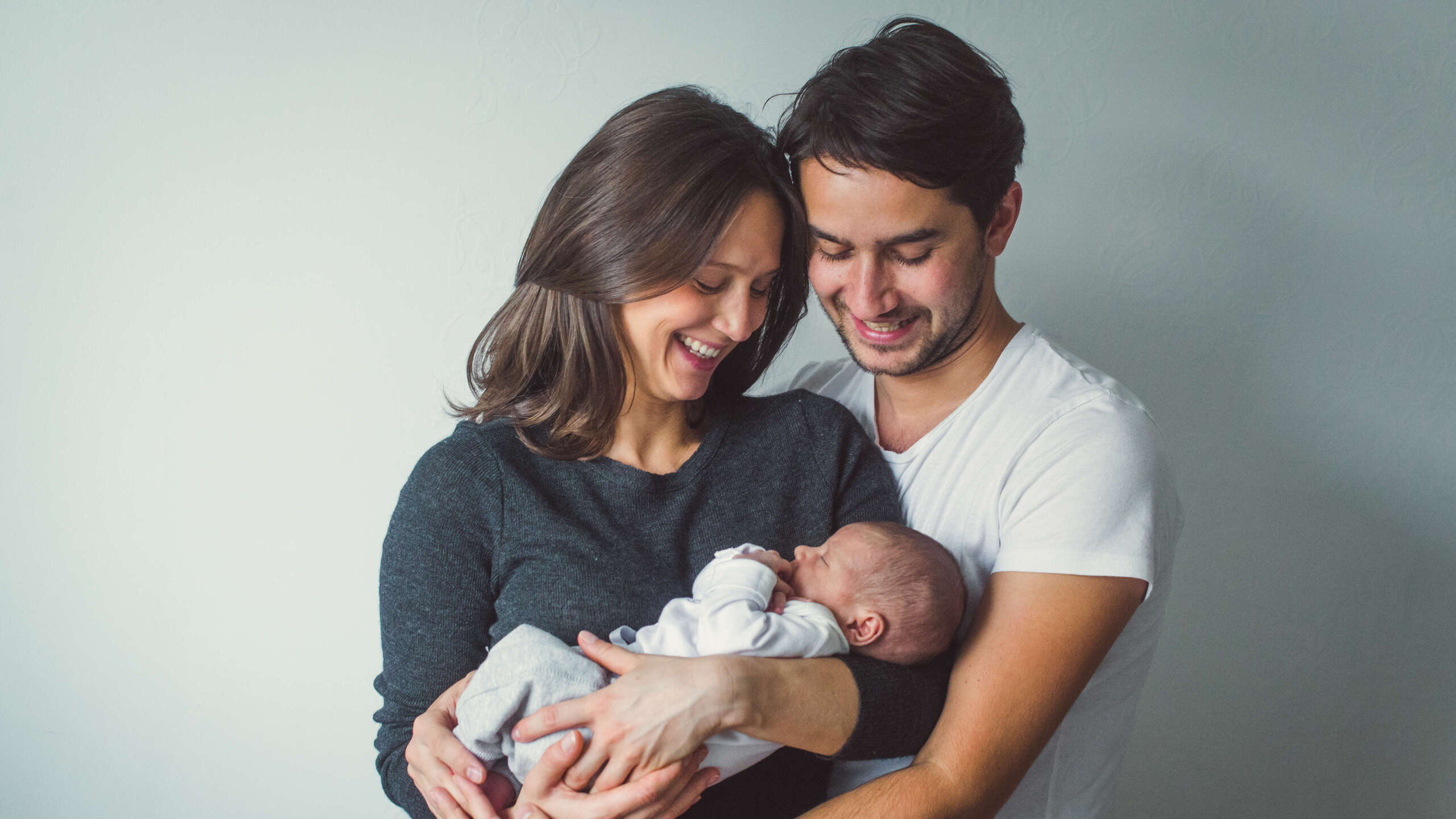 Young happy couple carrying and looking at their newborn child in hands 