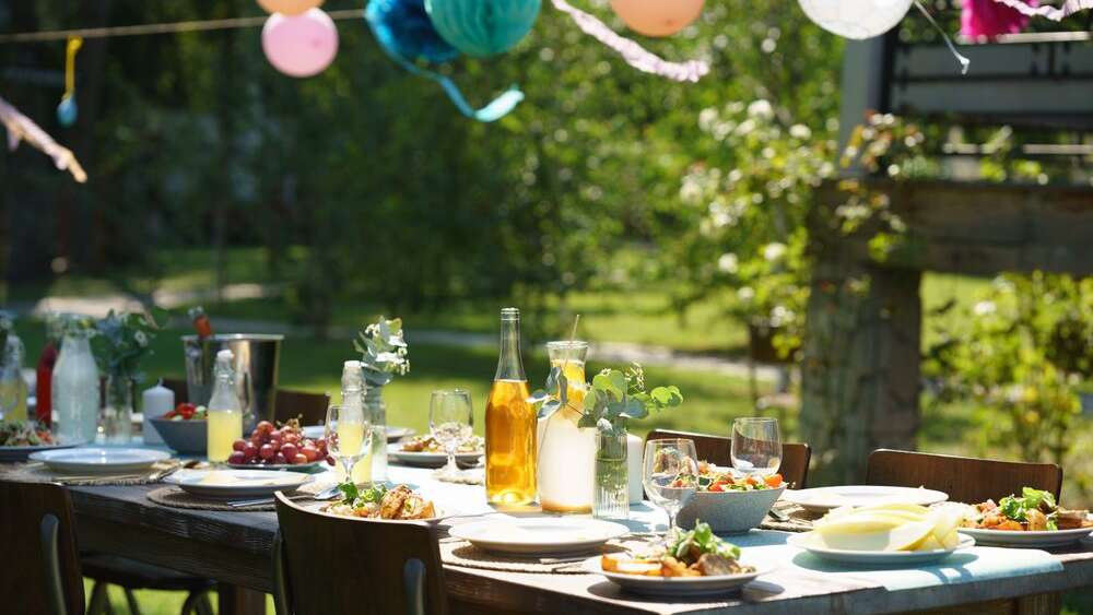 Close up shot of set table at baby shower party, grilled food and refreshments. Table setting with glasses, lemonade, delicate floral and paper decoration, and bottles of summer wine.