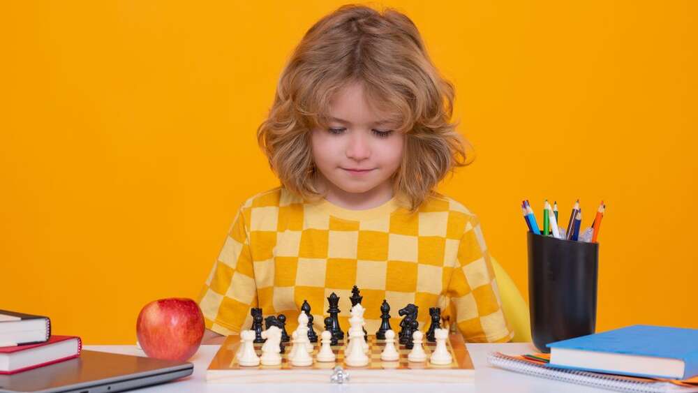 Kid playing chess. Clever child thinking about chess. Kids early development. Kid with chess on yellow isolated studio background.