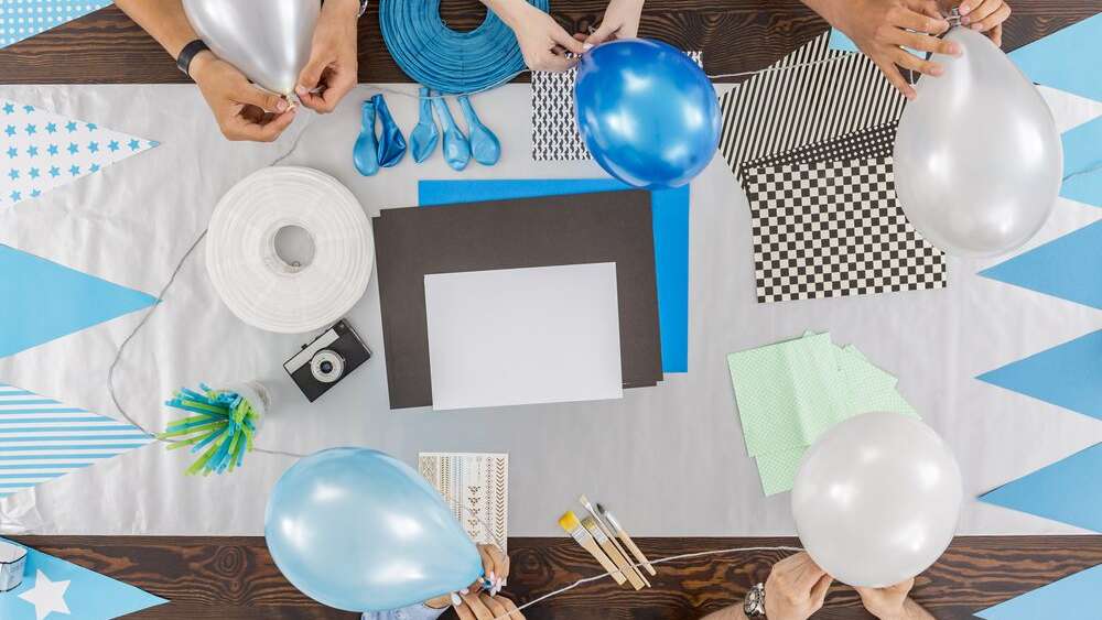 People prepping for the baby shower party by tying blue and white themed balloons