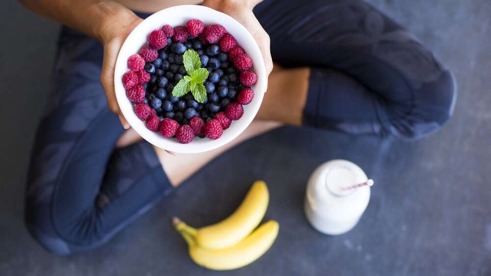 Close up of a bowl full of red and black berries topped with mint leaf